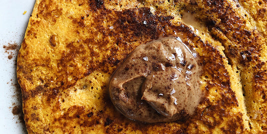 a photograph of a pancake made out of butternut squash on a white plate with a dollop of nut butter on top and sprinkled sea salt, cinnamon and medicinal mushroom maple syrup.