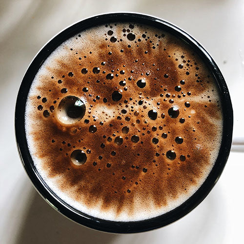 close up birds eye view of a coffee mug with a frothy milk thats bubbling. The milk is brown in the centre and turns white at the end giving a tye dye effect