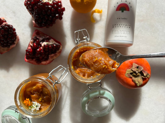 There are two jars open that have persimmon honey in them.  Next to them are two open pommegranates and a bottle of reishi