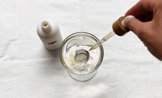 glass of water with a hand dropping in Rainbo's 11:11 tincture into the glass of water so that it can be drank.