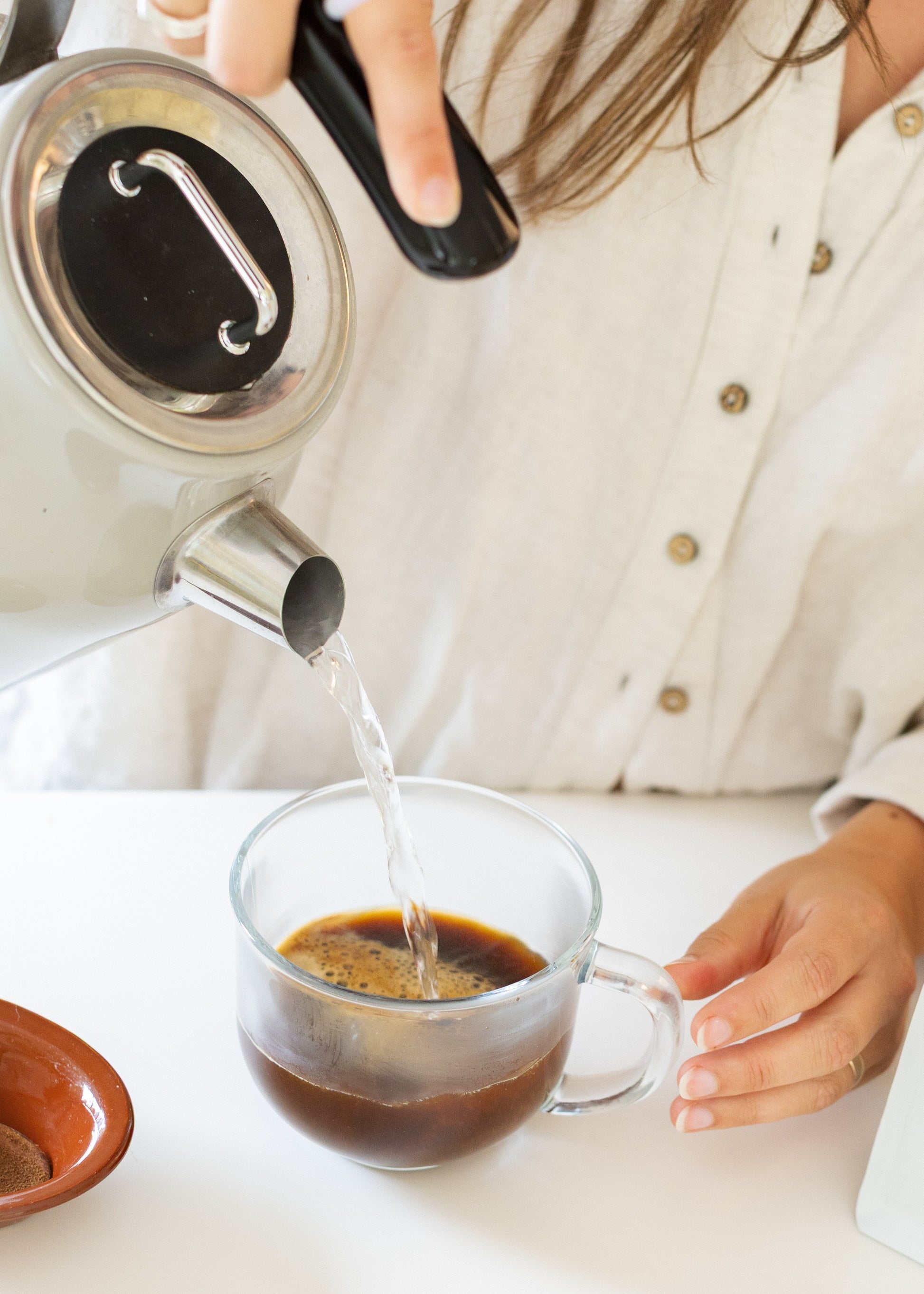 Person pouring water into a glass mug with Fungki Coffee powder in it.