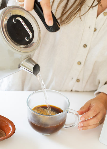 Person pouring water into a glass mug with Fungki Coffee powder in it.